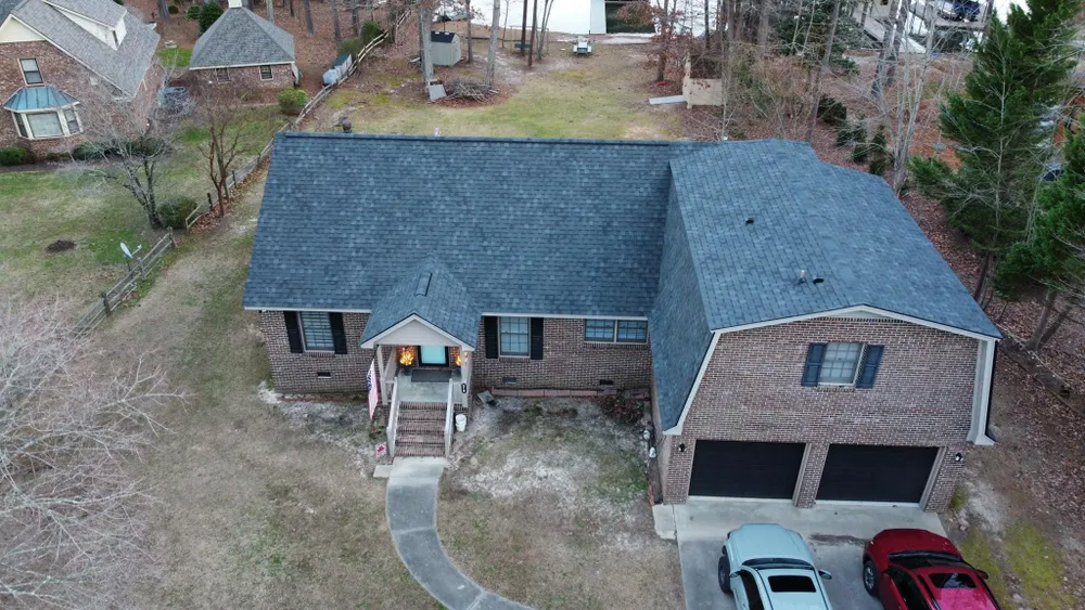 Aerial view of a suburban house with a dark roof, brick exterior, and two-car garage.
