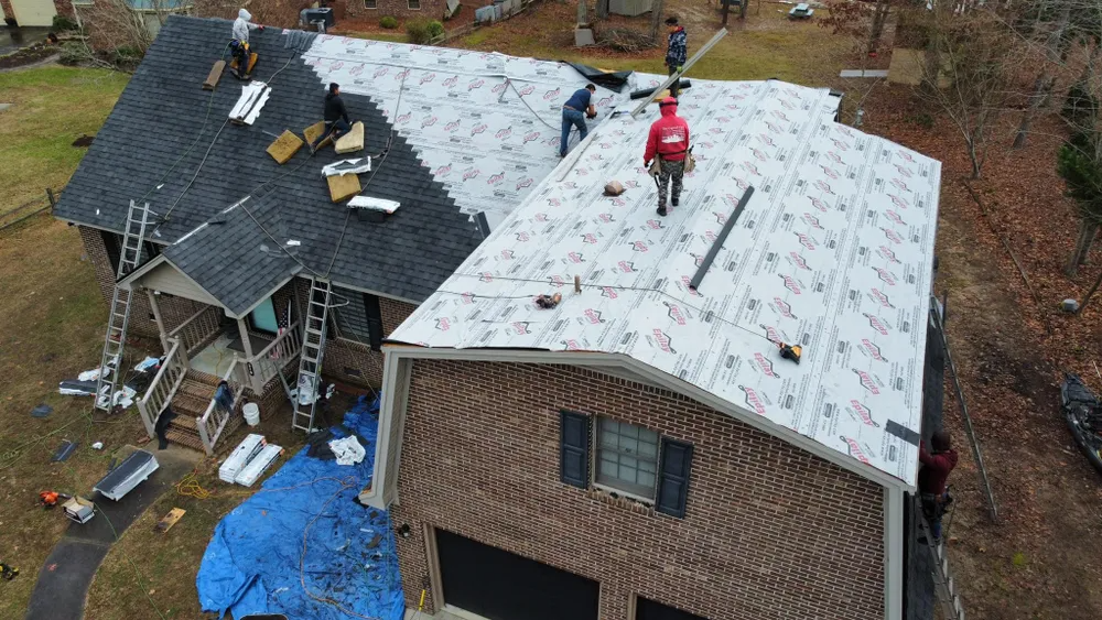 Workers repairing a roof, with underlayment exposed on a brick house.
