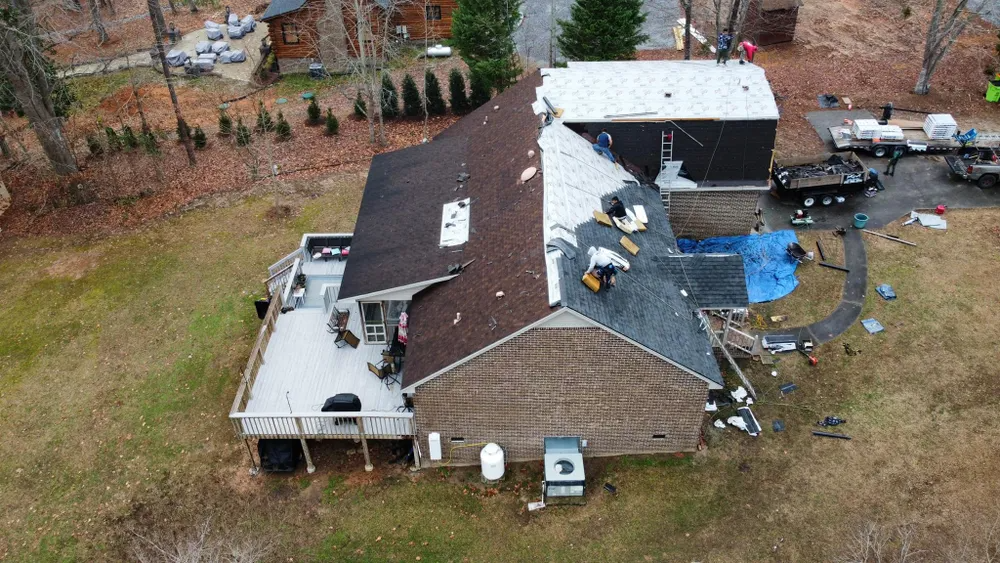 Aerial view of a house with roof damage and debris scattered around the yard after a storm.