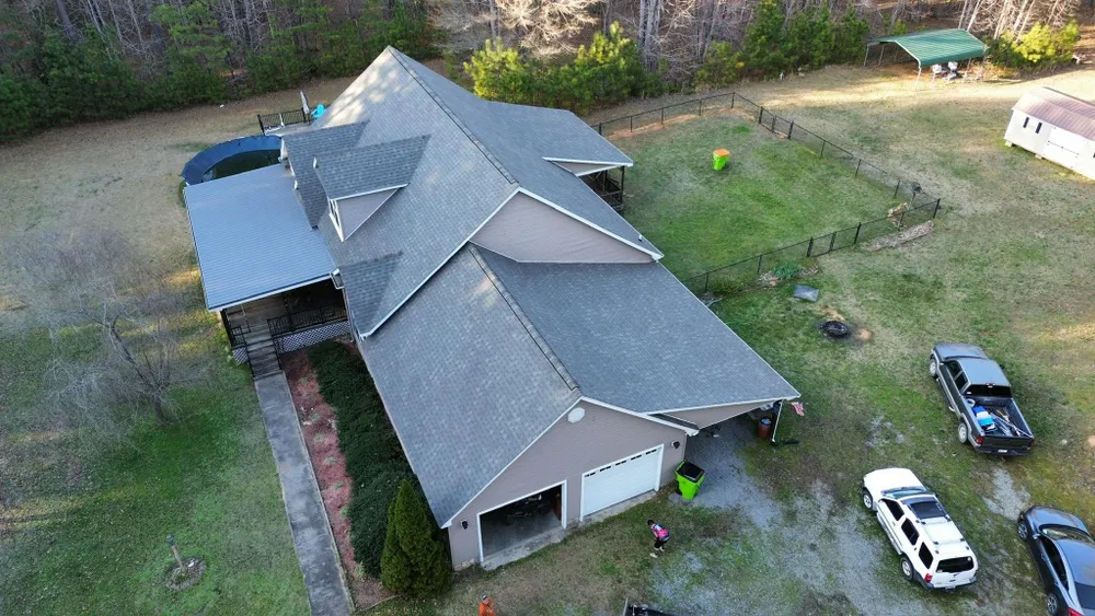 Aerial view of a large gray-roofed house with vehicles parked on a grassy yard.