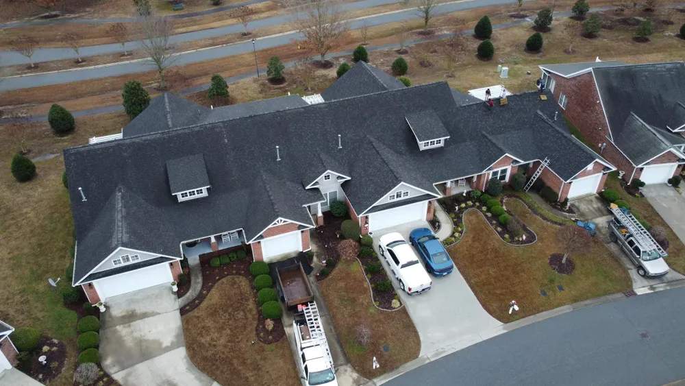 Aerial view of three suburban townhouses with driveways and parked cars beside a road.