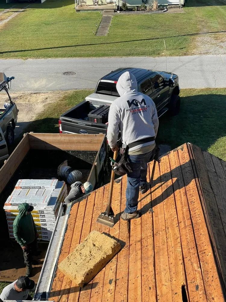 Worker on a roof near a black pickup truck, carrying shingles and tools.