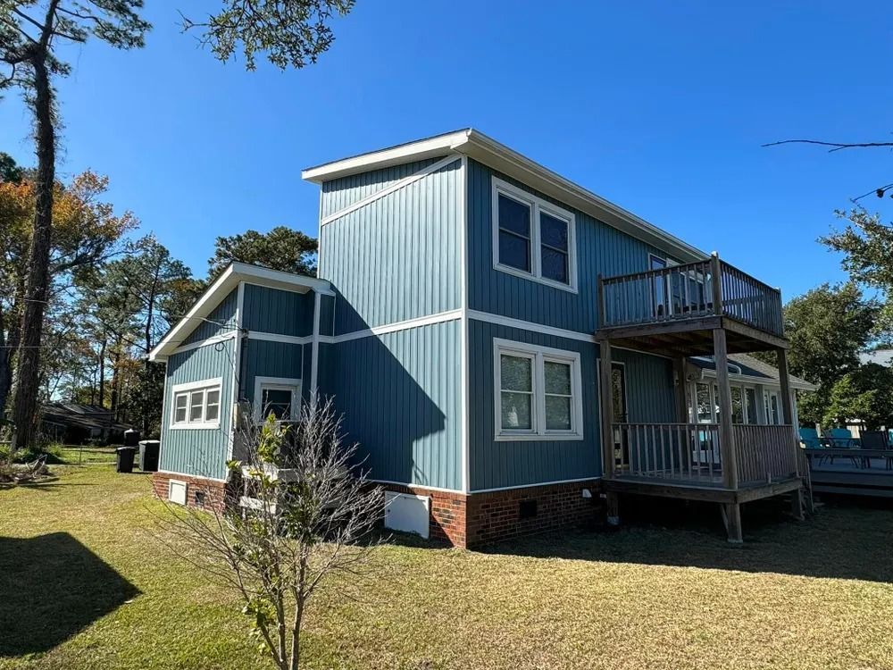Blue two-story house with white trim and a small porch on a grassy yard under a clear sky