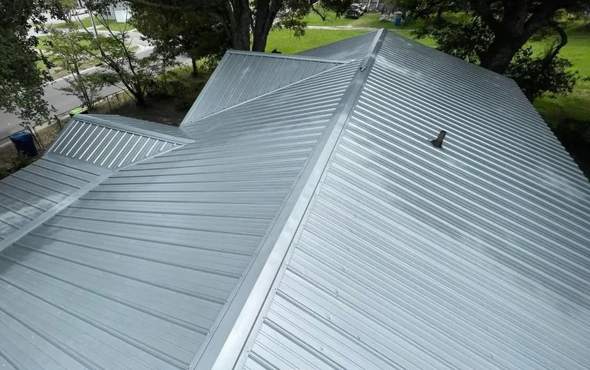 Silver metal roof with a ridge vent, seen from above among trees