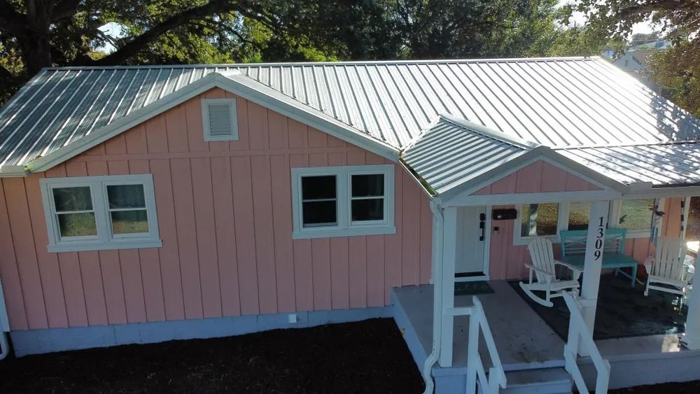 Pink house with white trim and green metal roof, viewed from above