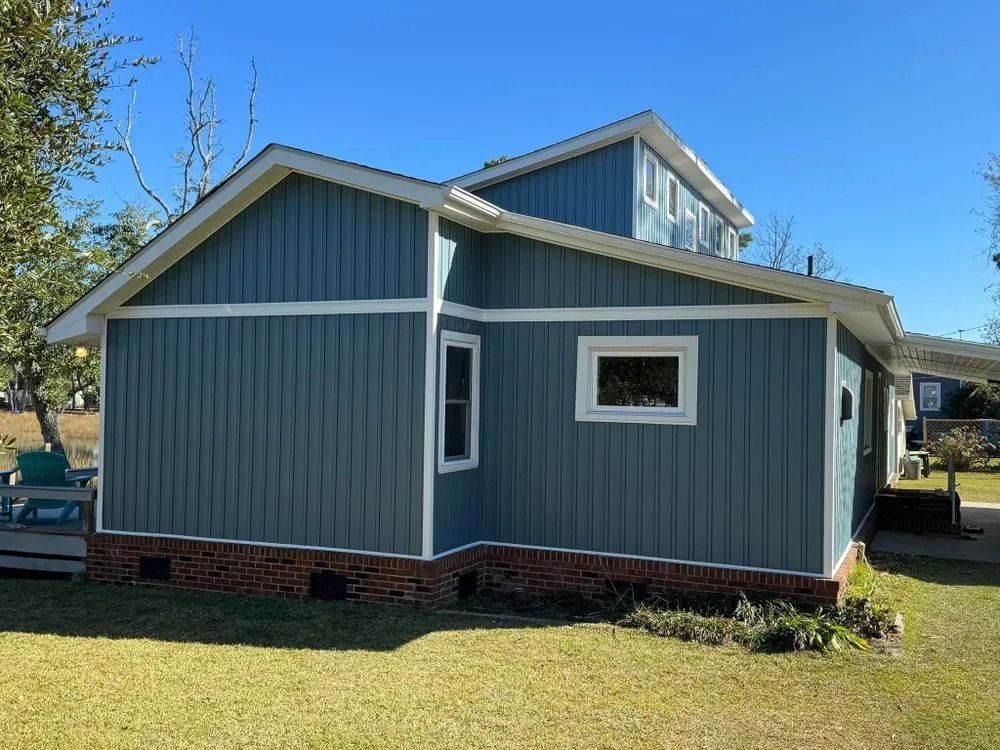Blue-gray house with white trim and brick foundation on a sunny lawn