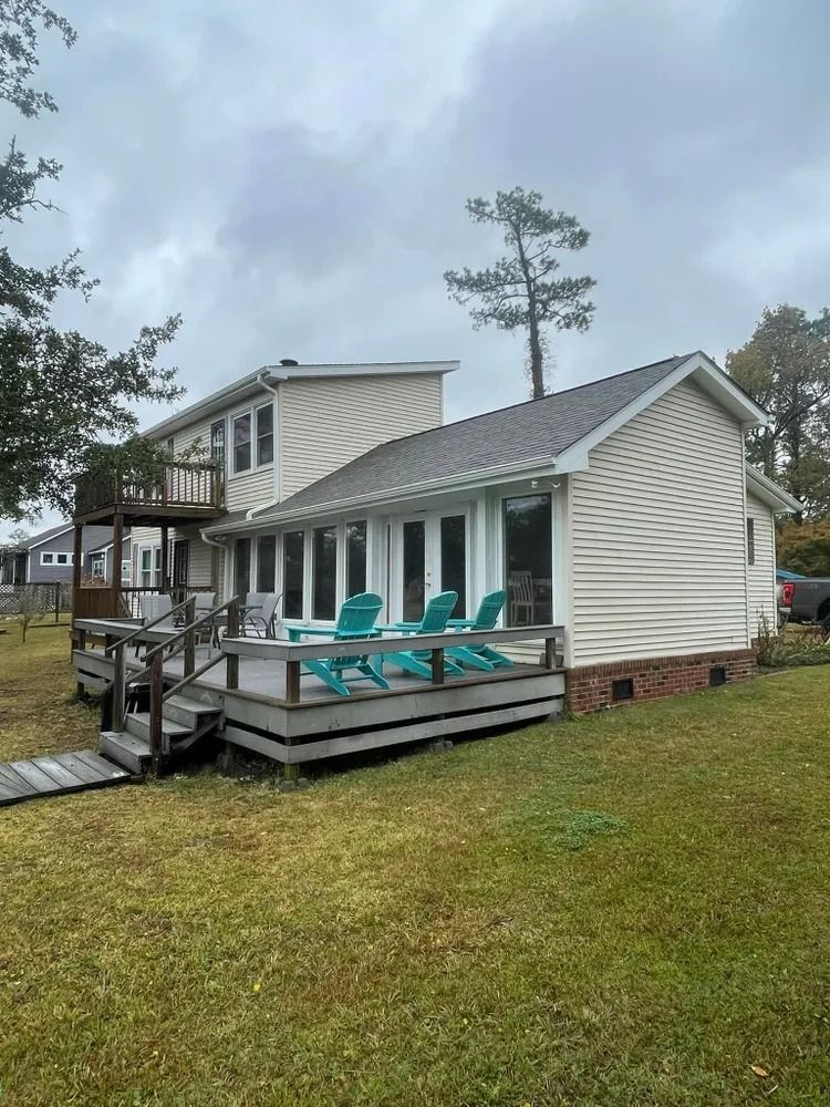 White house with gray roof, screened porch, and teal chairs on a grassy lot under cloudy skies