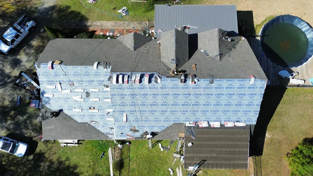 Aerial view of a house with a blue tarp roof, surrounded by trees and outbuildings.