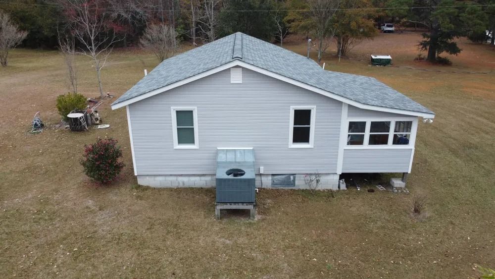 Gray single-story house with white trim and a small front porch, seen from above in a grassy yard.