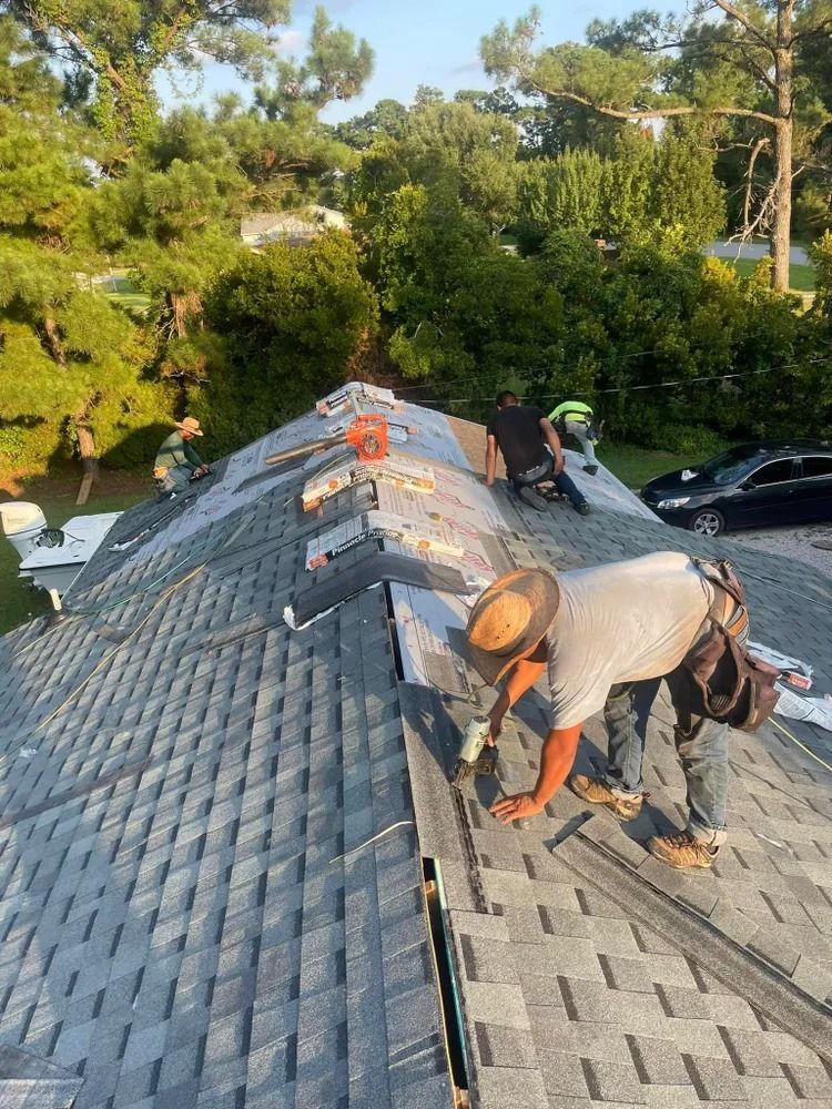 Workers installing gray shingles on a roof in a wooded neighborhood