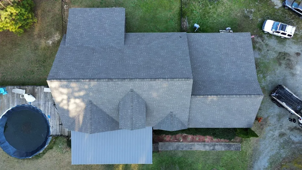 Aerial view of a house with a gray roof, trampoline on the left, and a parked white vehicle at the top right.