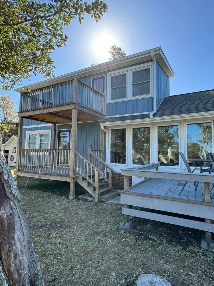 Blue two-story house with a front porch, stairs, and deck in a sunny yard