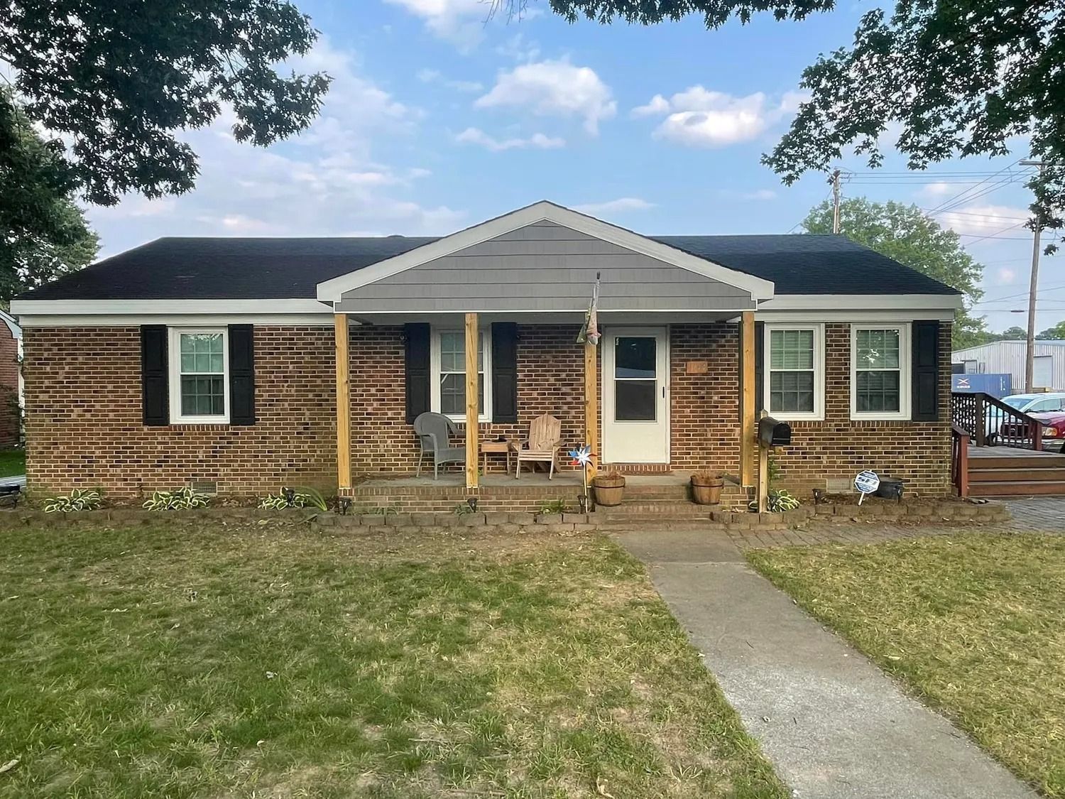 Single-story brick house with front porch, black roof, and a concrete walkway leading to the door