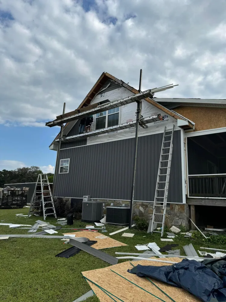 House exterior under repair with ladders, scaffolding, and construction materials on the lawn