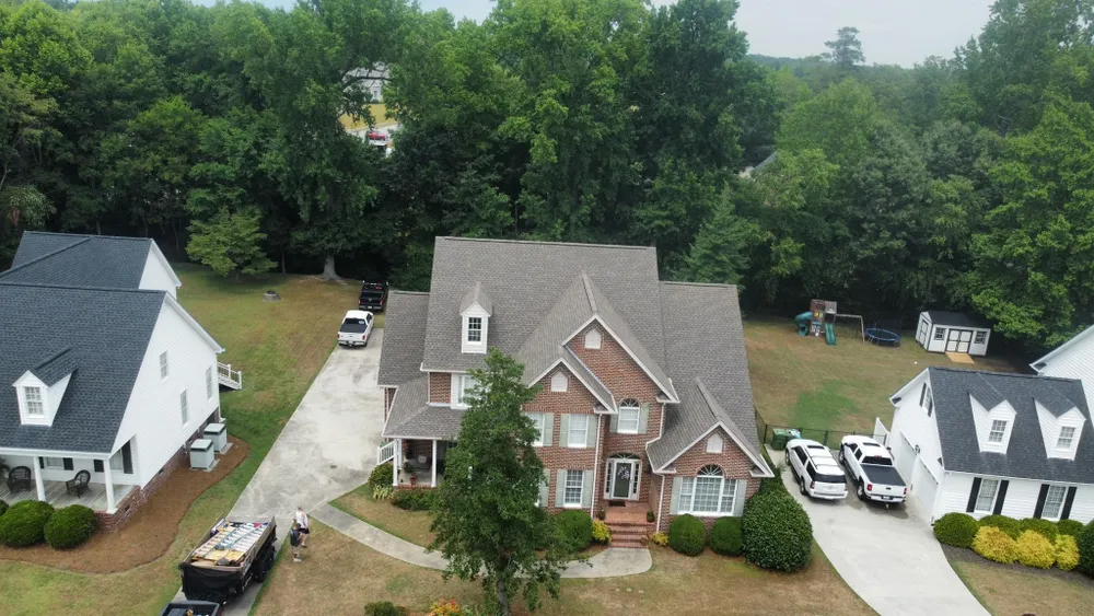 Aerial view of a suburban brick house with a driveway, trees, and neighboring homes