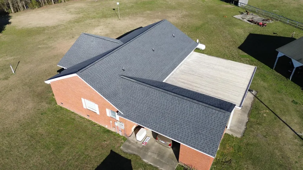 Aerial view of a brick house with a dark gray roof and a light-roofed extension on a grassy lot.