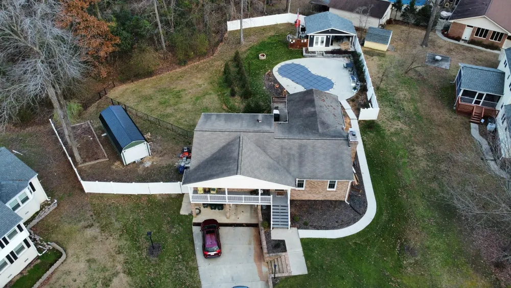 Aerial view of a suburban house with a driveway, backyard pool, and surrounding trees.