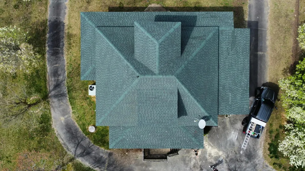 Aerial view of a house with a teal roof, driveway, and parked car beside it.