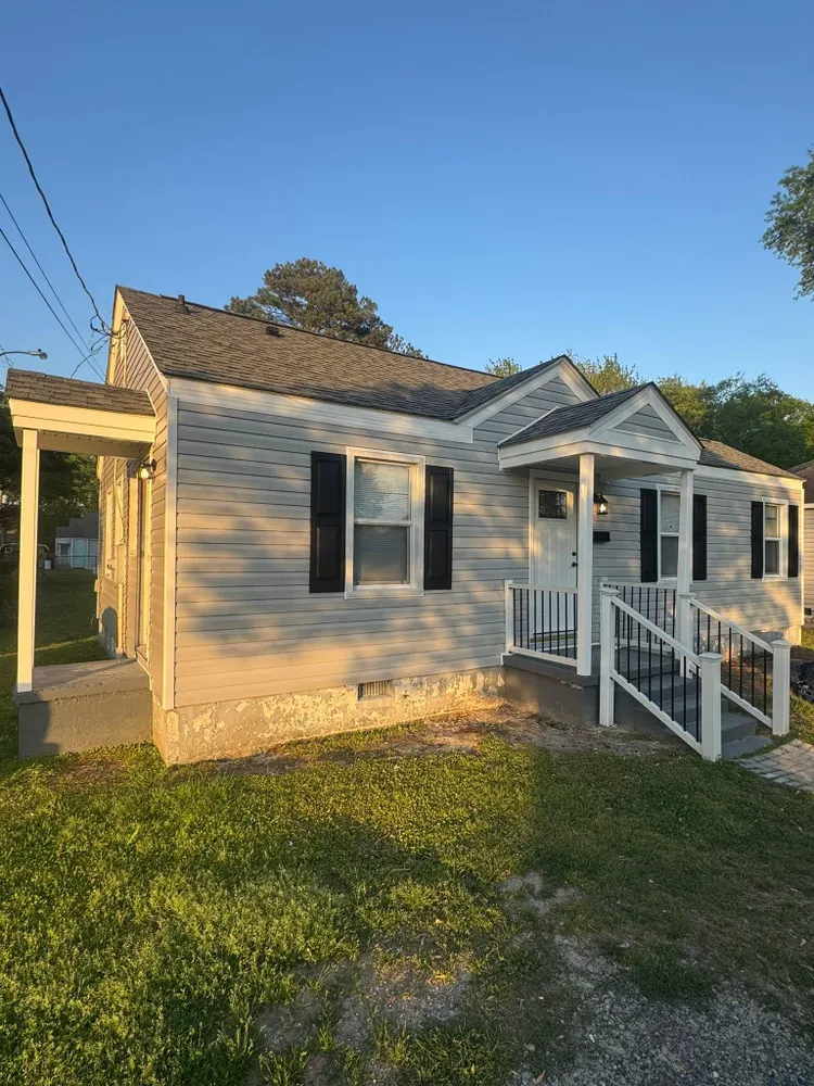 Small beige house with white porch and steps in a sunny yard