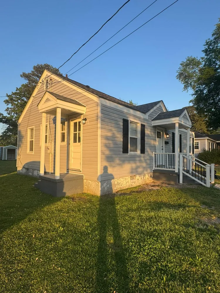 Sunlit yellow house with white porch and steps on a grassy lot at dusk