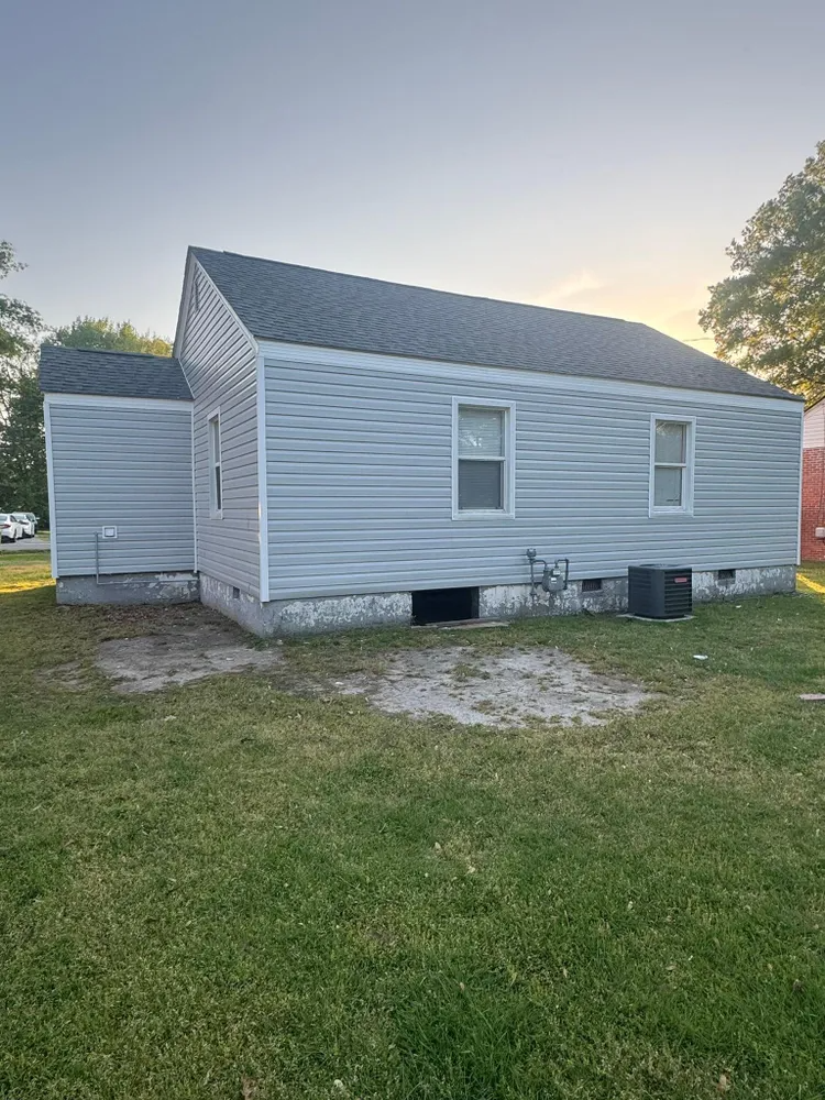 Small white house with gray roof, side addition, and a grassy yard at sunset.