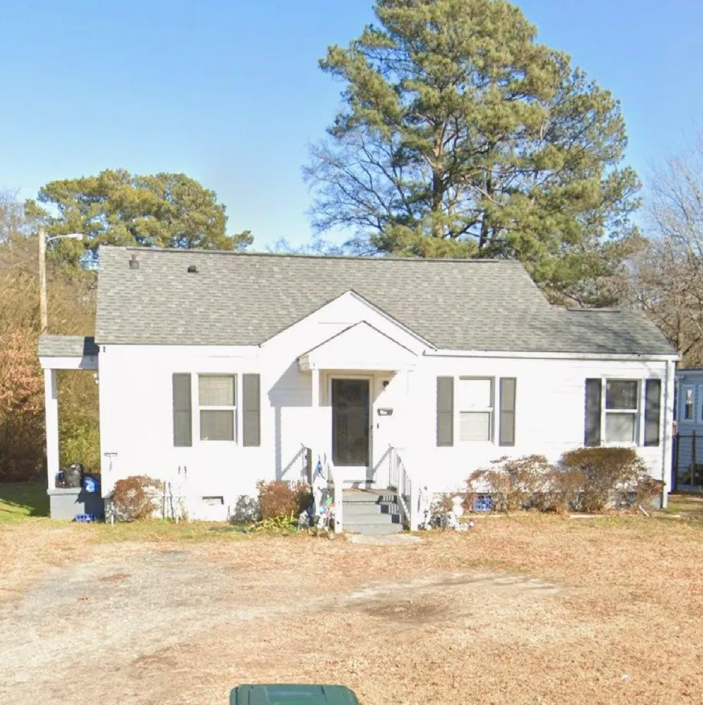 Small white house with gray roof, front steps, and yard under a clear blue sky