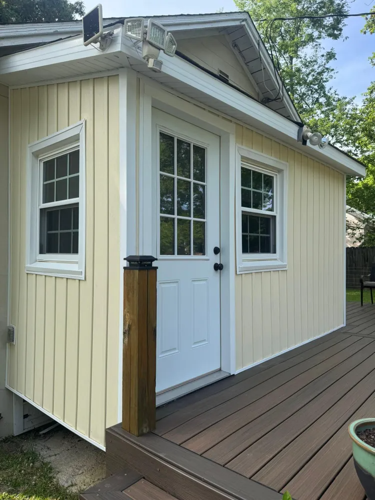 Small beige shed with white door and windows on a wooden deck outdoors