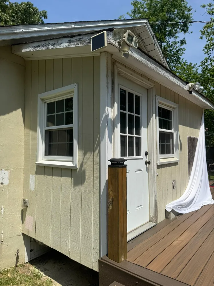 Small beige shed with white door and windows on a wooden deck in sunlight