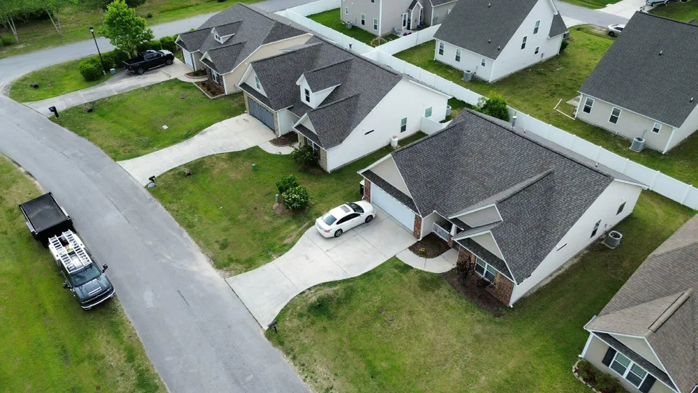 Aerial view of suburban homes, driveways, and parked vehicles on a quiet residential street.