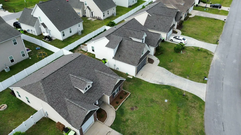 Aerial view of suburban houses, driveways, and green lawns along a curved street