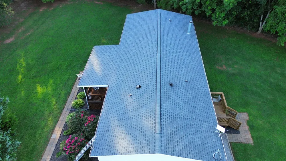 Aerial view of a gray-roofed house surrounded by green lawn and trees.