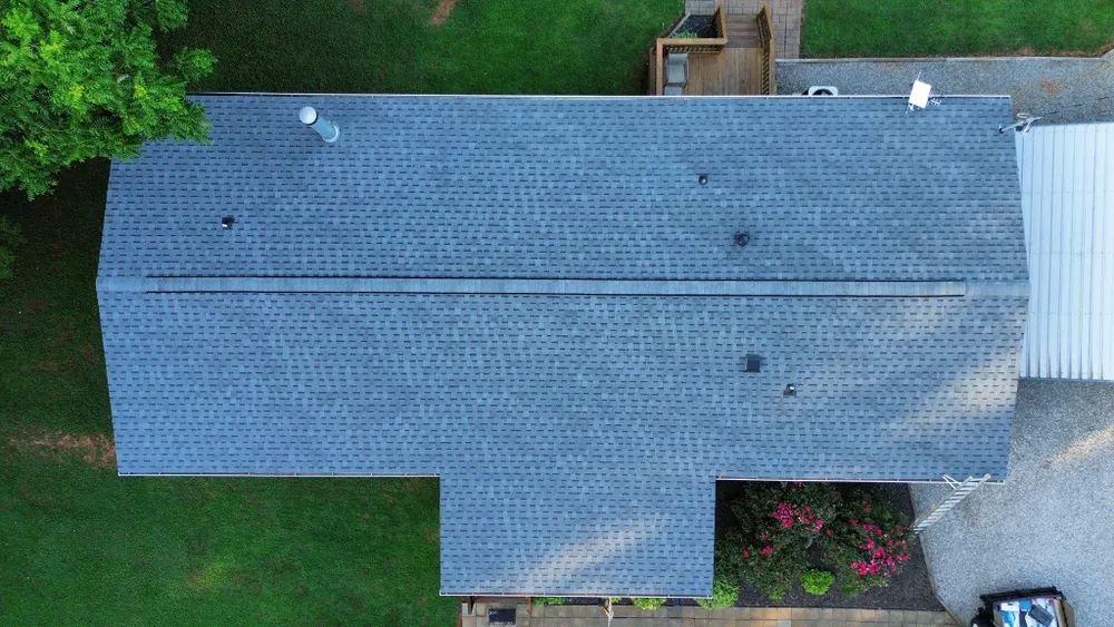 Aerial view of a gray-shingled roof with a small back porch, surrounded by green trees and yard.