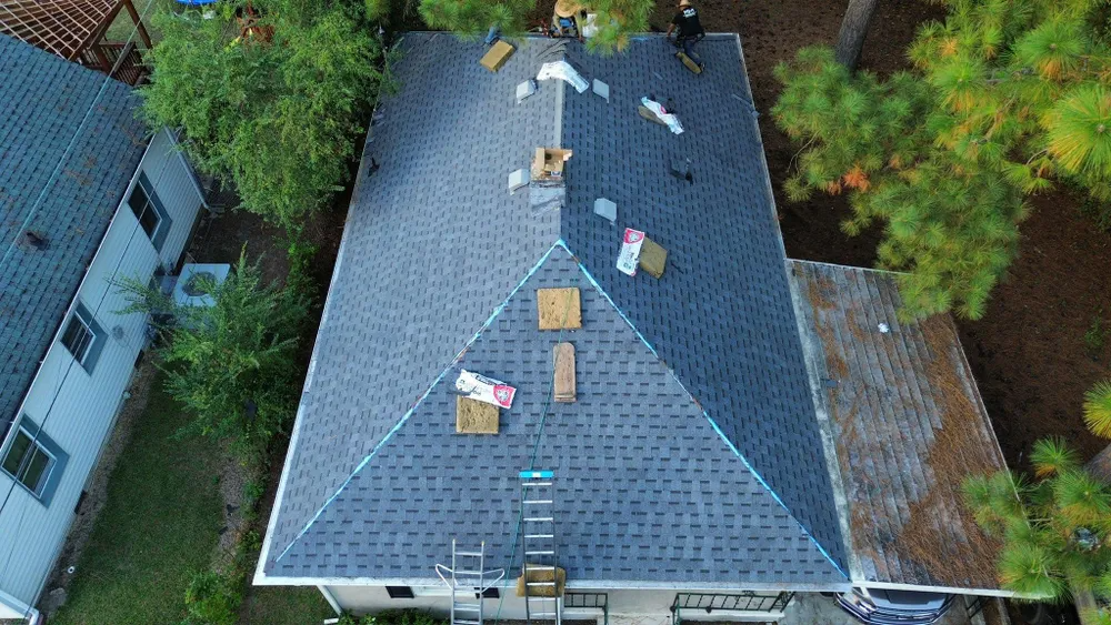 Aerial view of a gray roof with scattered equipment, surrounded by trees and neighboring houses.