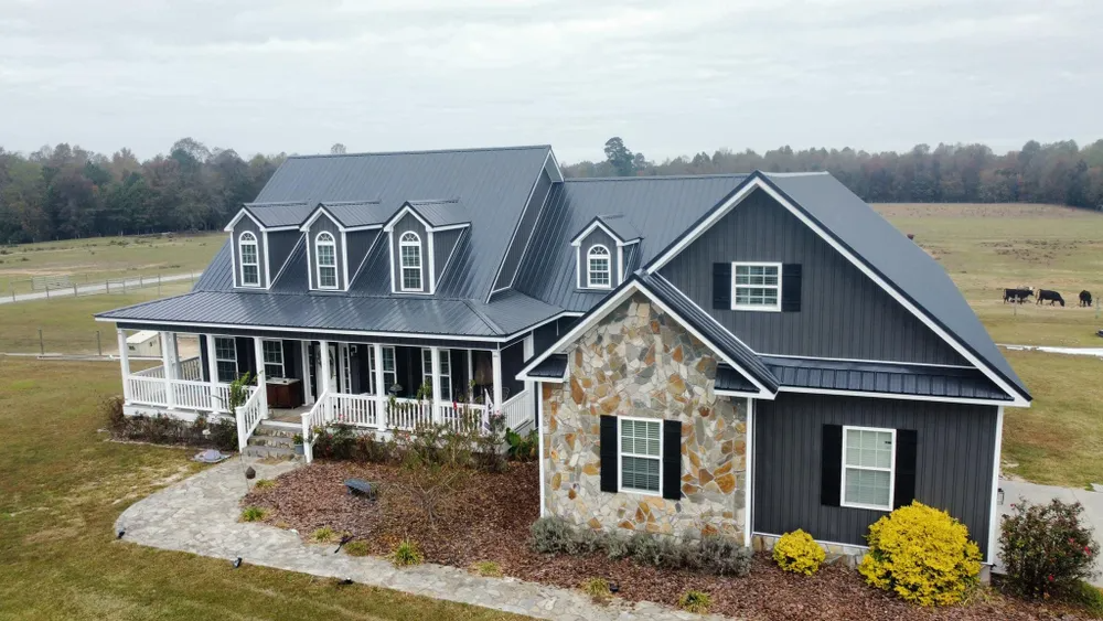 Large gray farmhouse with stone accents and covered porch in a rural field
