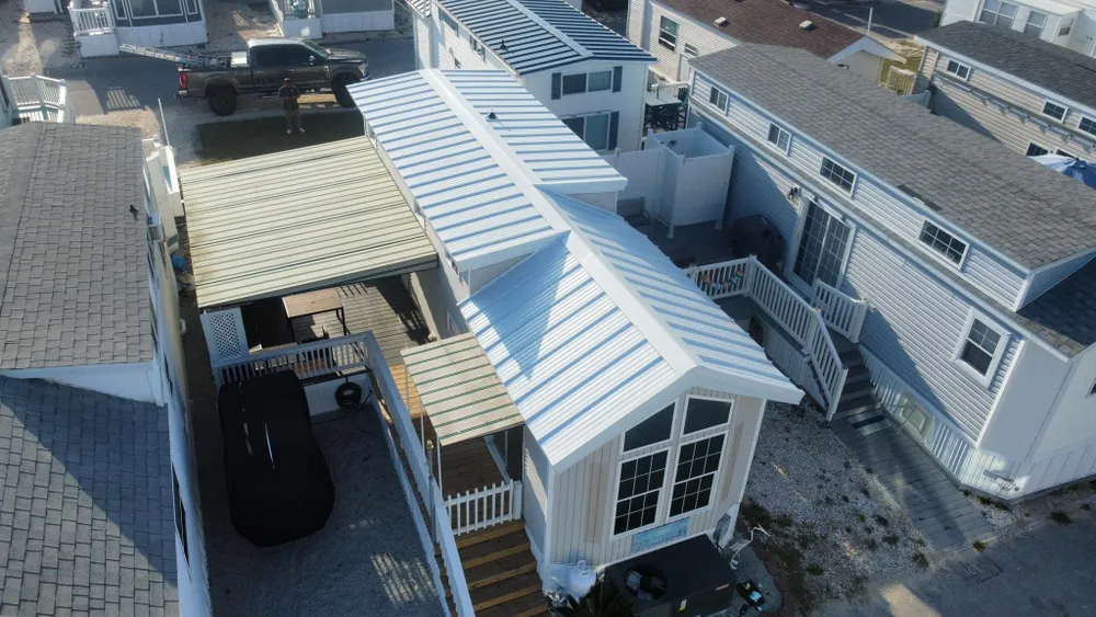 Aerial view of a house with white roof panels, a carport, and neighboring homes in a residential area