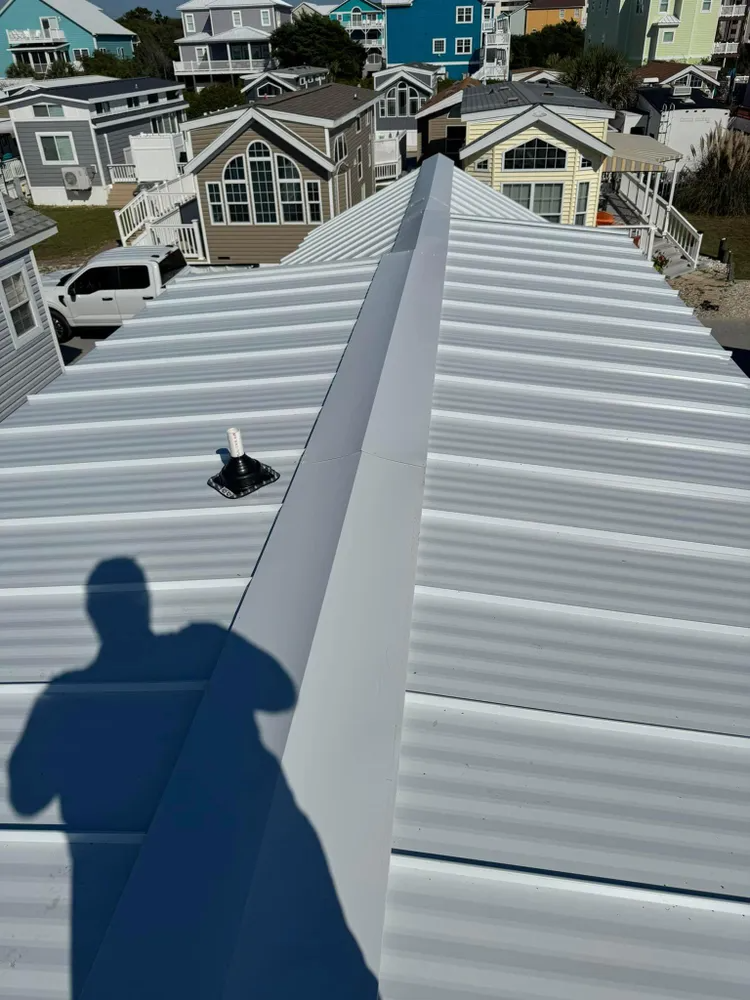 View from a metal roof ridge over neighboring houses on a sunny day, with a person’s shadow in the foreground