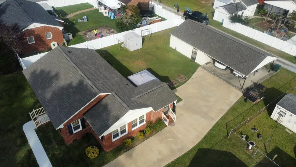 Aerial view of a suburban house with a driveway, lawn, and neighboring homes behind white fences.