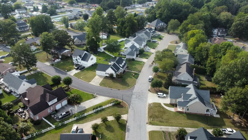 Aerial view of a quiet suburban neighborhood with houses, tree-lined streets, and green lawns.