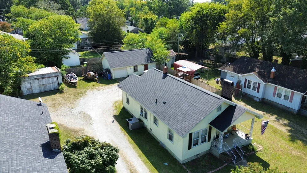 Aerial view of several small houses and outbuildings along a gravel driveway, surrounded by trees and green lawns.