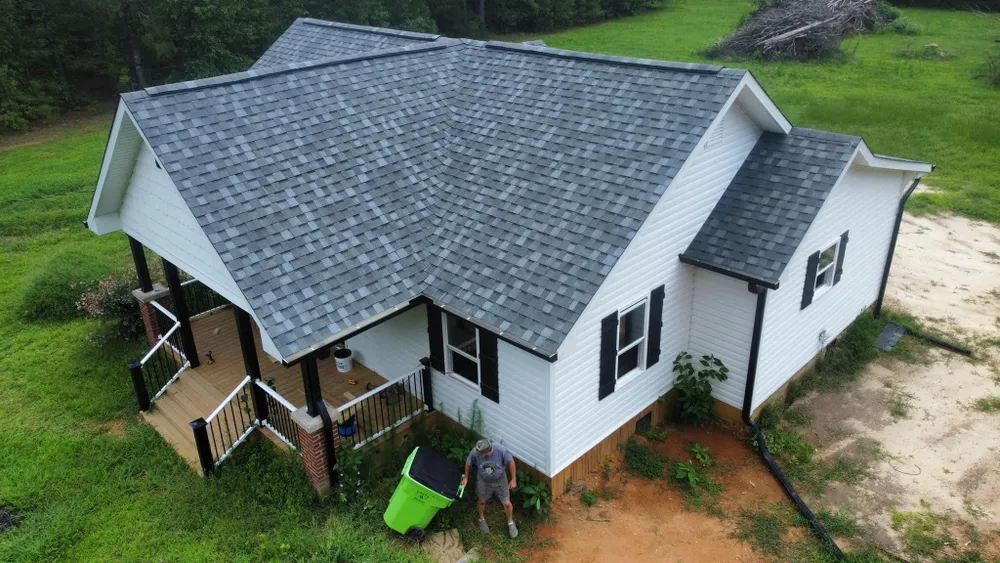 Aerial view of a white house with a gray roof, wooden deck, and green lawn in a rural setting