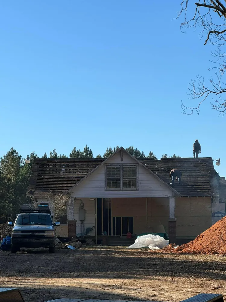 House under renovation with a truck parked in front and roof debris on the ground