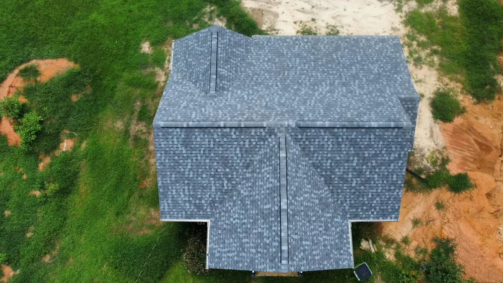 Top-down view of a gray shingled house roof surrounded by green grass and patches of bare dirt