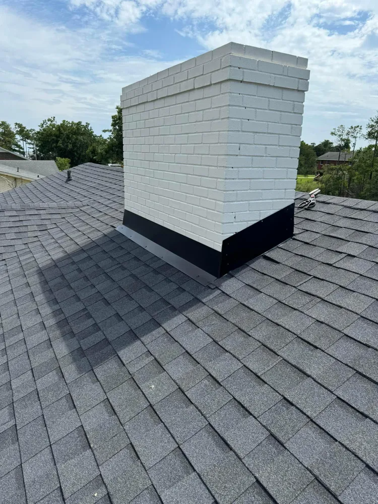 White brick chimney on gray shingled roof under a partly cloudy sky