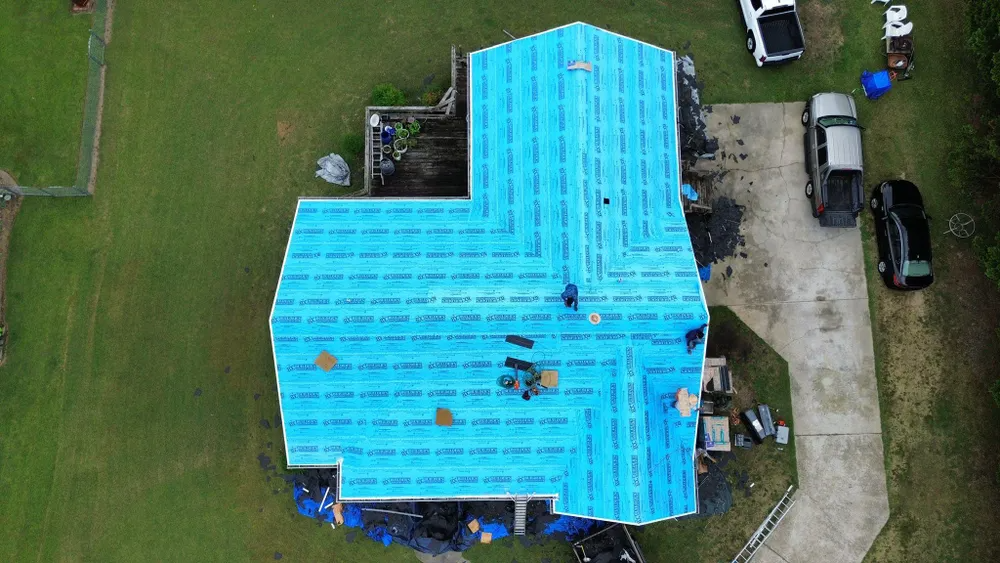 Aerial view of a house roof covered in bright blue tarp with people working on repairs below.