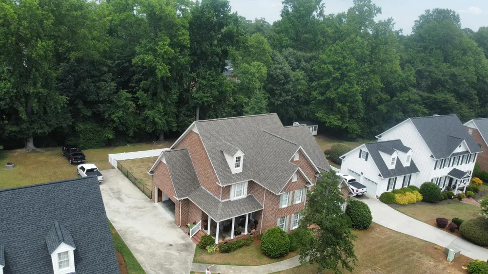 Aerial view of a brick suburban house with a gray roof, driveway, and surrounding trees