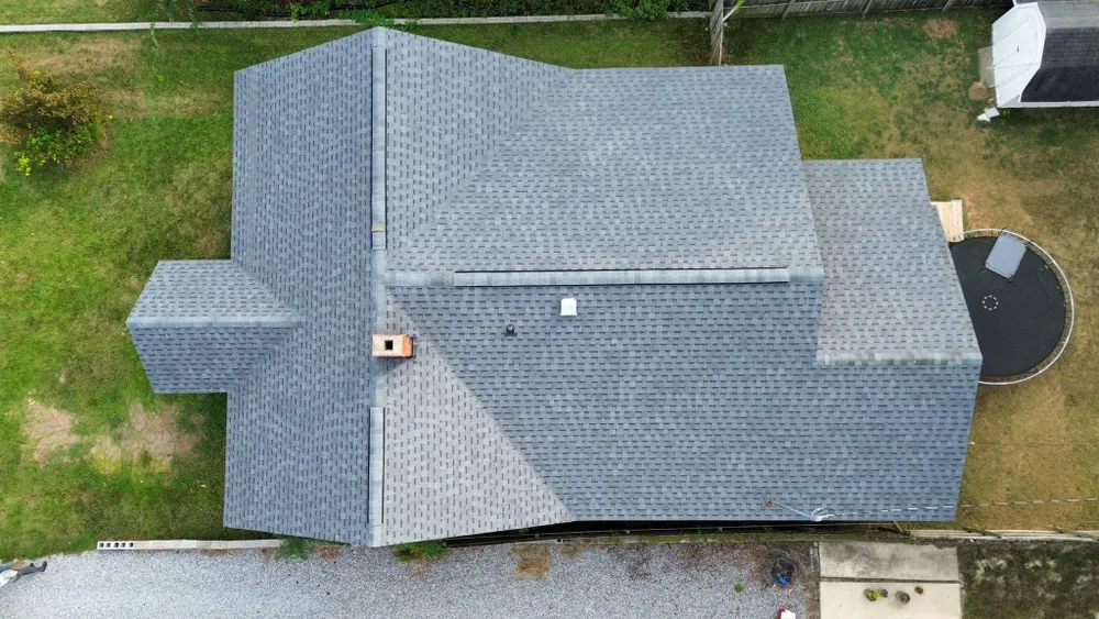 Aerial view of a gray-shingled house roof beside a grassy yard and driveway.