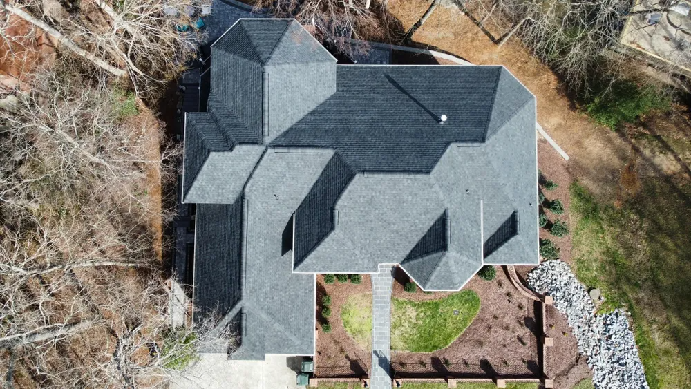 Aerial view of a house with a dark gray roof, trees around it, and a small backyard patio.