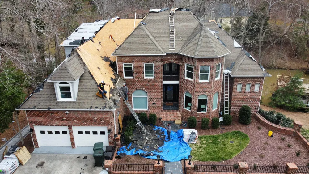 Aerial view of a house with major roof damage and a blue tarp covering debris in the backyard.