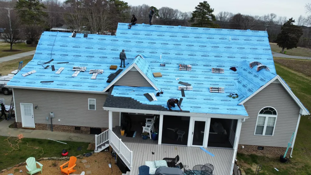 House with new blue roof under construction, viewed from above, with workers and materials visible