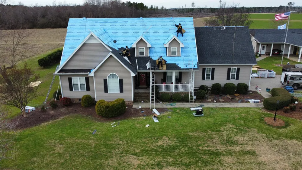 Suburban house with a blue roof, front porch, and landscaped yard on a cloudy day